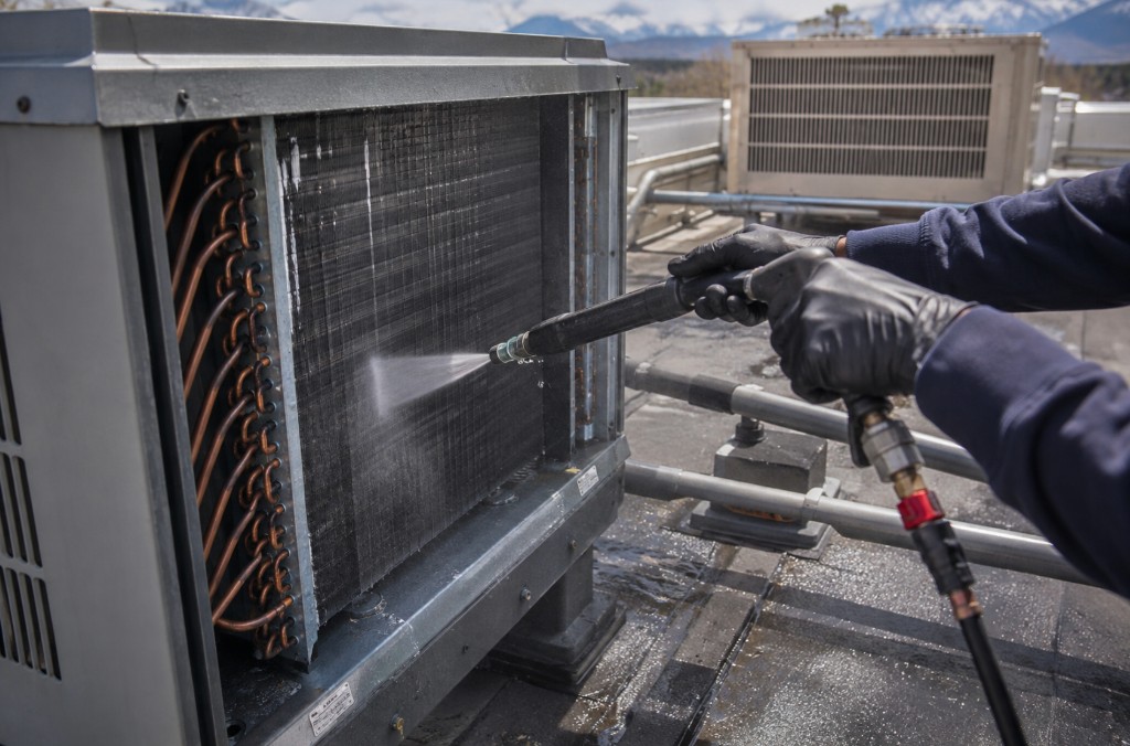 Technician pressure-washing commercial HVAC coil fins on a Colorado rooftop